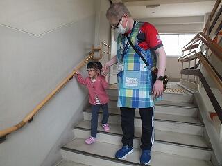 幼児が手すりをつかんで、教師の手引きで階段を下りている。 幼児が手すりをつかんで、教師の手引きで階段を下りている。