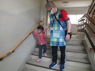 幼児が手すりをつかんで、教師の手引きで階段を下りている。
